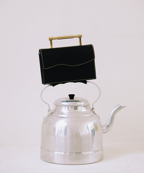 Editorial photo of black vegan structured bag with with top-stitching and gold sleek top handle