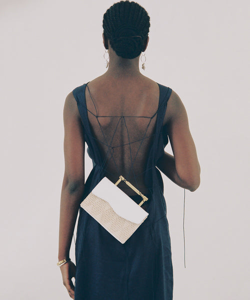 Editorial image of rectangular, structured bag with golden art deco-inspired top handles. White and raffia coloured summer bag.