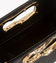 A minimalist, black leather handbag with a sculptural gold-tone handle opening, featuring an asymmetrical organic design.